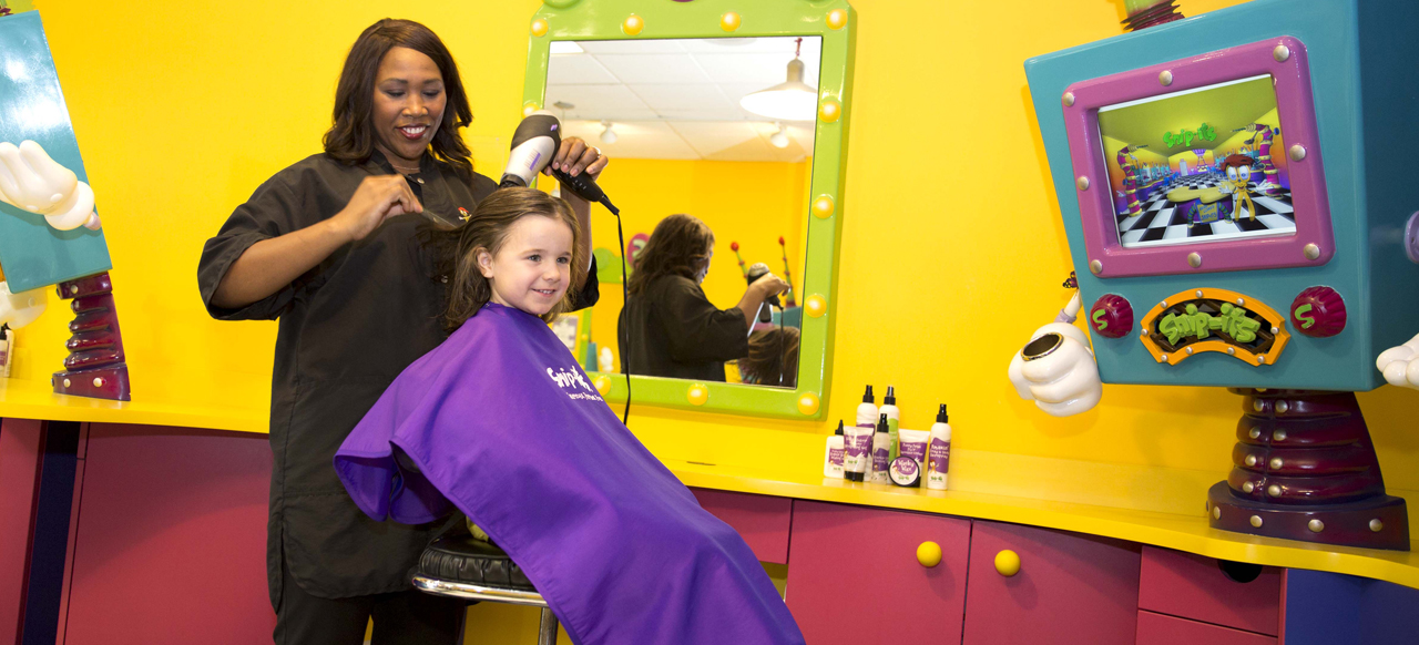 A young girl enjoying her haircut experience with a stylist at Snip-its.