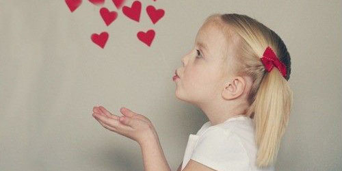 The profile of a young girl with pig tails blowing kisses to red hearts in the air.