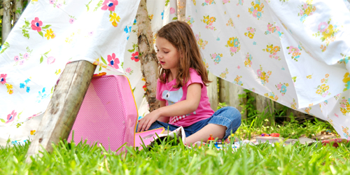 A young girl playing outside in a fort made of floral bedding sheets.